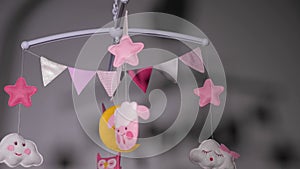 baby mobile with pink hand-stitched animal and bird toys with yellow moon on white wall background.