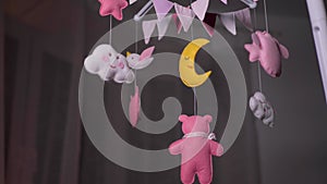 baby mobile with pink hand-stitched animal and bird toys with yellow moon on white wall background.