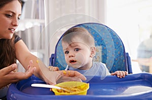 Baby, mother and feeding food in kitchen or vegetable nutrition in high chair or breakfast eating, development or hungry