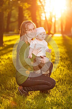 Baby with mother in the park in the rays of sunset. Toddler with mom on the nature outdoors. Backlight. Summertime family scene