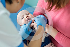 Baby on mothers hand at hospital. Nurse making infant oral vaccination against rotavirus infection. Children health care