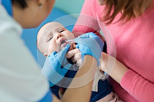 Baby on mothers hand at hospital. Nurse making infant oral vaccination against rotavirus infection. Children health care photo