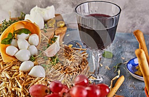 Baby mozzarella cheese on a hay with garlic and grapes, a glass of red wine on a blue background