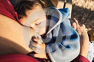 Baby naps while being breastfed by his mother outdoors