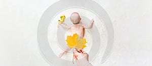 Baby newborn child banner. Mother hand holding yellow leaf. Happy cute baby kid girl lying on white bed background. Cute
