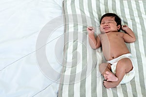 Baby newborn girl is 1-month-old, half-Thai half-Nigerian, laying and crying in a white bed
