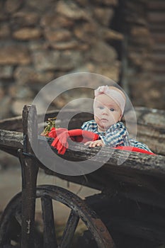 Baby newborn girl with blue eyes wearing tartan check dress shirt and pink shawl bandana posing on wooden old style retro wagon ca photo