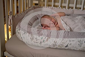 A baby newborn is sleeping in a baby cocoon with a burning night light. A child is an infant in a home crib by the light of a