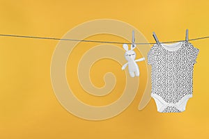 Baby onesie and bunny toy drying on laundry line against orange background, space for text