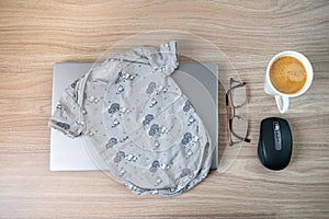 Baby onesie, coffee, glasses laptop on wooden table indoors symbolising maternity or parental leave