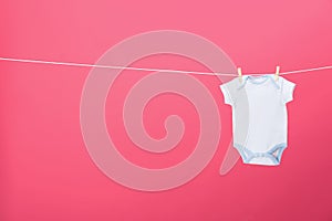 Baby onesie hanging on clothes line against background, space for text