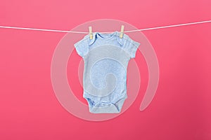 Baby onesie hanging on clothes line against pink background