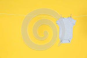 Baby onesie hanging on clothes line against yellow background