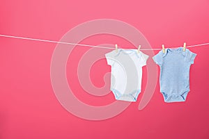 Baby onesies hanging on clothes line against pink background