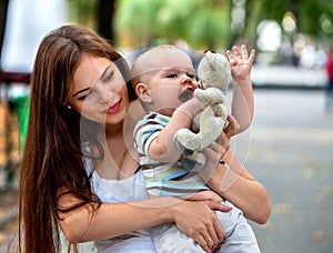 Baby in park outdoor. Kid with toy on mom`s hands.