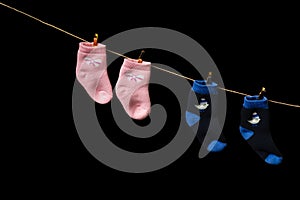 Baby Pink and blue socks hang on a pin on a rope. On a black background