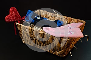 Baby Pink and blue socks and heart lie in a basket on the hay, on a black background.