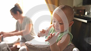 baby is playing around in the kitchen. baby is standing on the feeding table, playing around and not wanting to eat