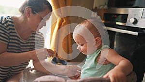 baby is playing around in the kitchen. baby is standing on the feeding table, playing around and not wanting to eat. mom