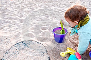 Baby playing with buckets and plastic toy shovels in a sandbox