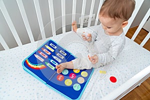 Baby playing with busy book sitting in crib. Concept of smart books and modern toys