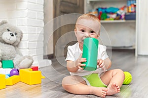 A baby is playing on the floor. The boy is sitting on the floor. The child takes the toy into his mouth and licks it