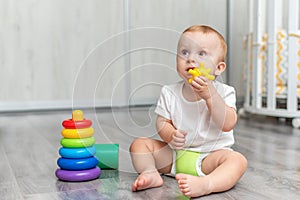 A baby is playing on the floor. The boy is sitting on the floor. The child takes the toy into his mouth and licks it