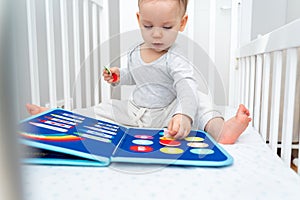 Baby playing with montessori busy book sitting in crib. Educational books and quiet books concept. Montessori busy board