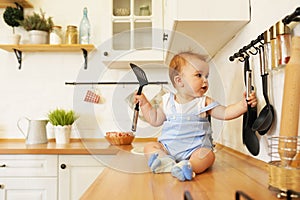 Baby playing with pans and spoons on kitchen table. One year old toddler infant hitting metal utensil