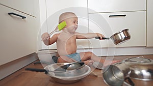 baby playing pots in the kitchen on the floor. happy family kid dream concept. baby scattered pots play dabble sitting