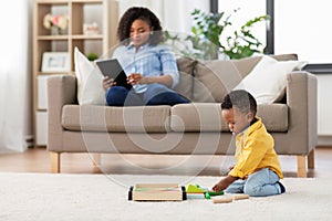 Baby playing toy blocks and mother using tablet pc