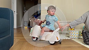 Baby plays bike indoors. Happy family a kid dream concept. Baby girl riding a children's scooter in the room indoors