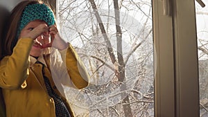 Baby plays sitting on the windowsill on the background of snow-covered trees.