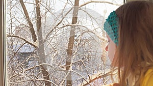 Baby plays sitting on the windowsill on the background of snow-covered trees.