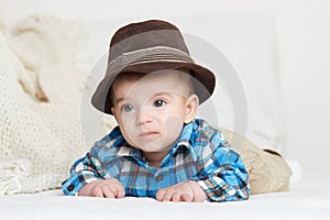 Baby portrait lie on white towel in bed, dressed in plaid shirt and hat