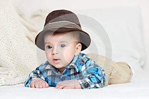 Baby portrait lie on white towel in bed, dressed in plaid shirt and hat