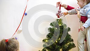 Baby and pregnan mom hang red ball toy on Christmas tree. happy childhood concept. child and mother decorate tree with