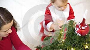 Baby and pregnan mom hang red ball toy on Christmas tree. happy childhood concept. child and mother decorate tree with