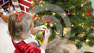 Baby and pregnan mom hang red ball toy on Christmas tree. happy childhood concept. child and mother decorate tree with