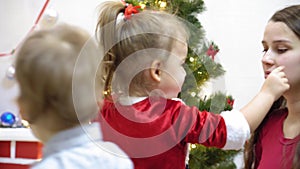 Baby and pregnan mom hang red ball toy on Christmas tree. happy childhood concept. child and mother decorate tree with