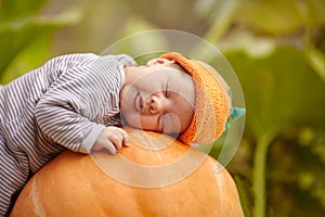 Baby with pumpkin hat sleeping on big orange pumpkin