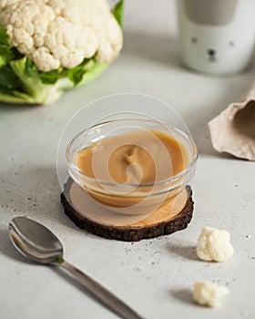 Baby puree in a cauliflower plate with a spoon, next to fresh cauliflower. Layout Baby food concept, first feeding.