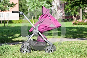 Baby pushchair is folded in lying position on green meadow in summer sunny park, side view, infant perambulator series