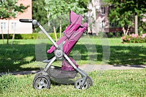 Baby pushchair is folded in seated position on green meadow in summer sunny park, side view, infant perambulator series