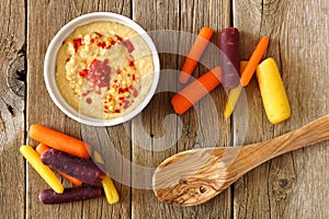 Baby rainbow carrots with hummus, overhead view on rustic wood