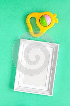 Baby rattle and photo frame on green background