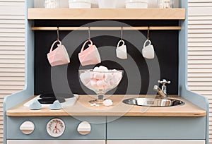 Baby retro kitchen with sink and stove, pink marshmellows in vase, pink and white cups on blackboard wall