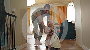 Baby rides a motor scooter indoors. Dad rides his son teaches him to ride a scooter around the room at home. Happy