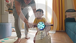 Baby rides a motor scooter indoors. Dad rides his son teaches him to ride a scooter around the room at home. Happy