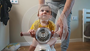 baby rides a motor scooter indoors. dad rides his son teaches him to ride a scooter around the room at lifestyle home